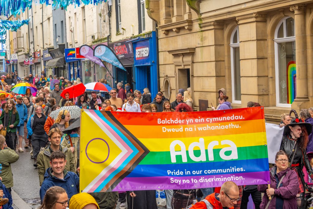 Photo of the Caernarfon Pride parade, with the Adra banner being held up.