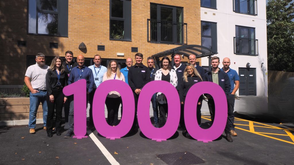 Picture of the development team outside Plas Penrhos, with big numbers 1000