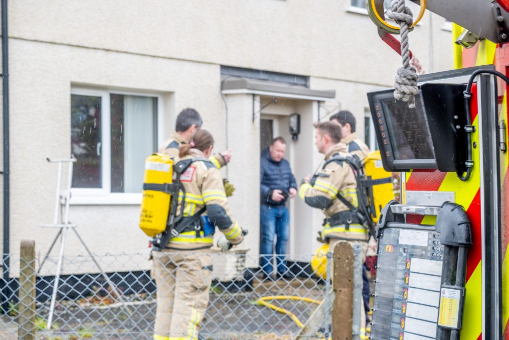 Four fire officers standing outside a house, with the resident of the house standing in the doorway.